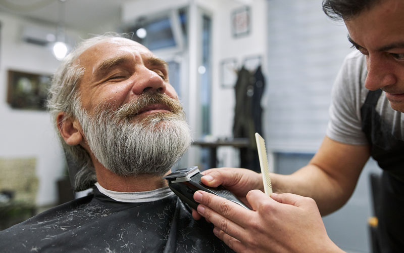 barber-salon Man receiving a beard trim at a barbershop with a relaxed expression on his face.
