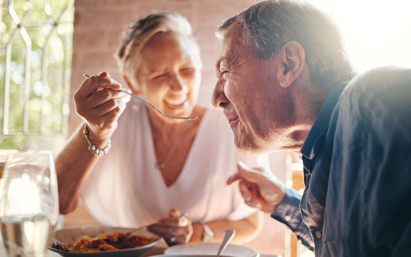seniors-dining Elderly couple enjoying a meal together, with the woman feeding the man a spoonful of food.