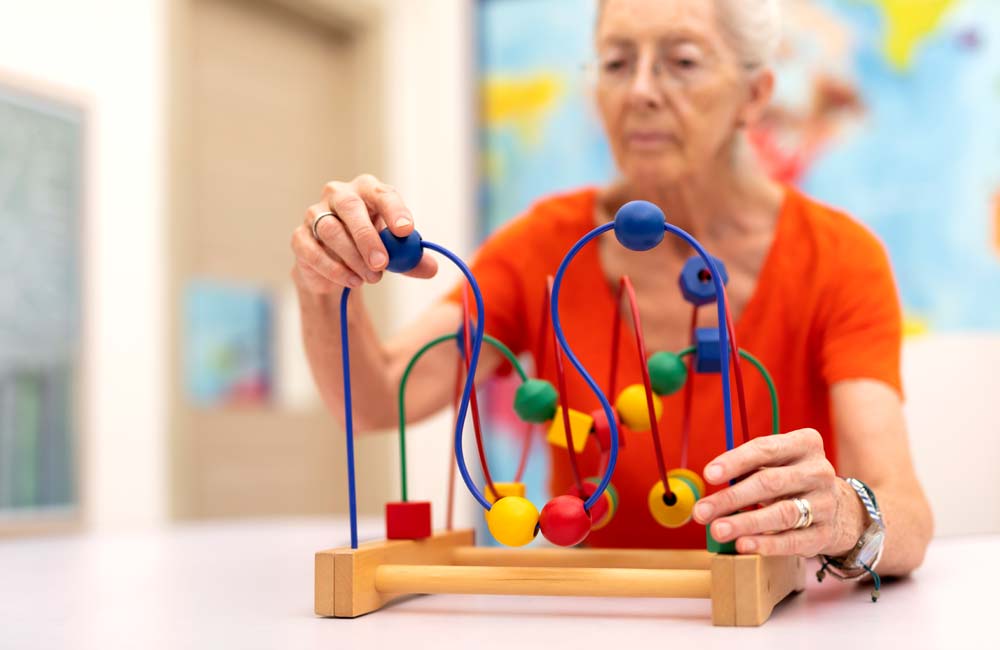 senior-memory-care--activity Elderly woman engaging with a bead maze toy during a memory care activity session.