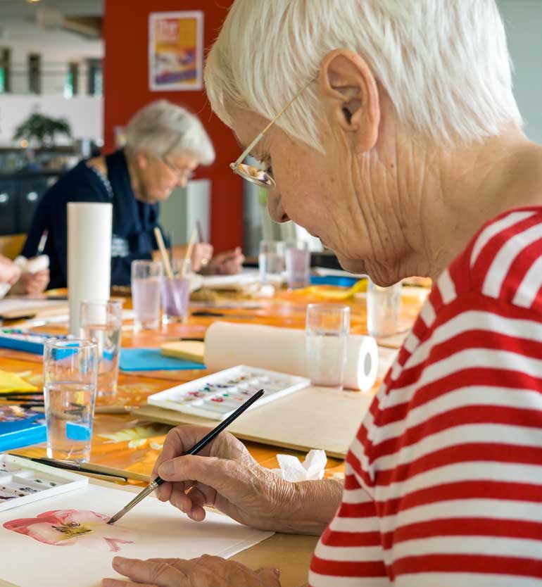senior-painting Elderly women engaged in watercolor painting at a table filled with art supplies