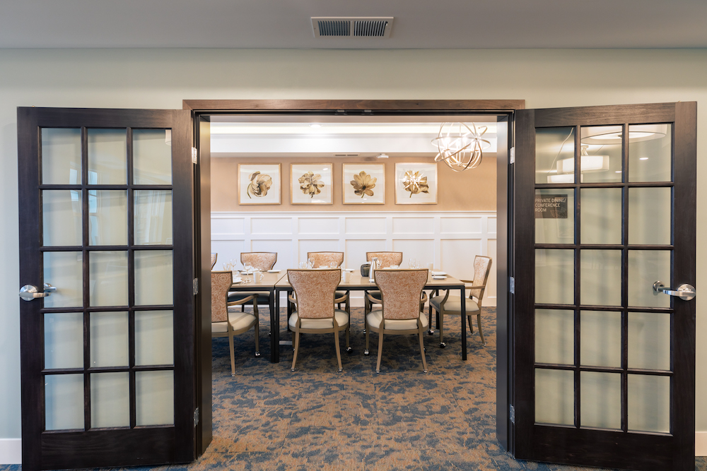 An elegant private dining room with framed botanical art, seen through open double doors with glass panels.