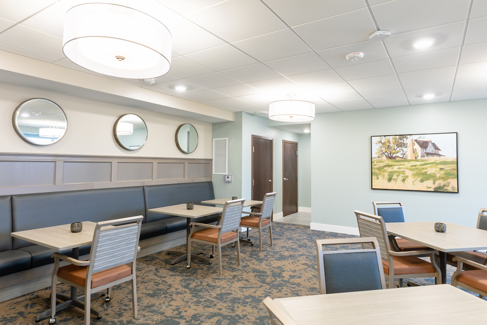 Modern dining area with sleek tables, chairs, round mirrors, and a landscape painting on the wall.