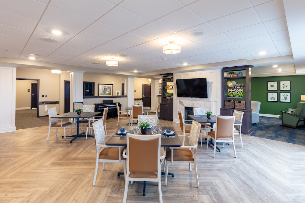 A modern dining area with tables, chairs, and a TV in a well-lit room with wooden flooring.