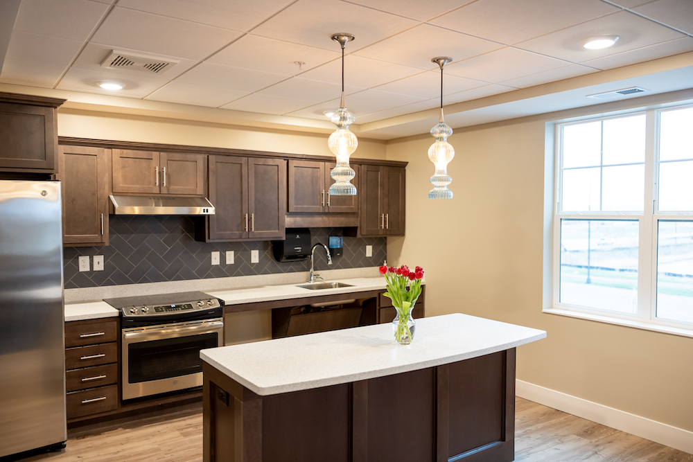 Modern kitchen interior with dark wood cabinets, island, pendant lights, and a vase of red flowers.