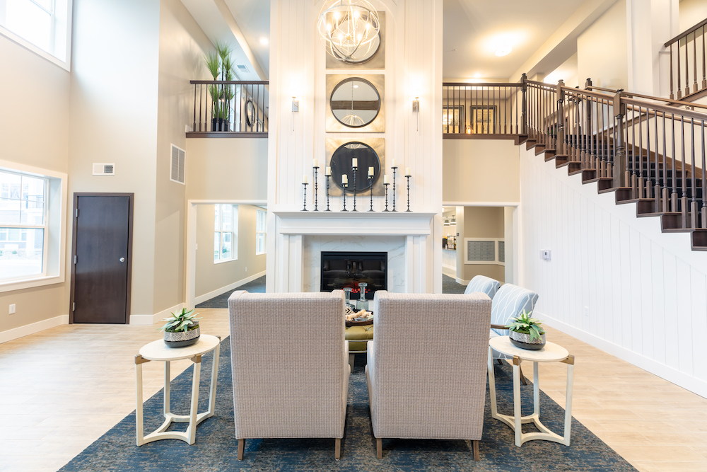 Spacious modern living room with high ceilings, two armchairs, fireplace, and staircase