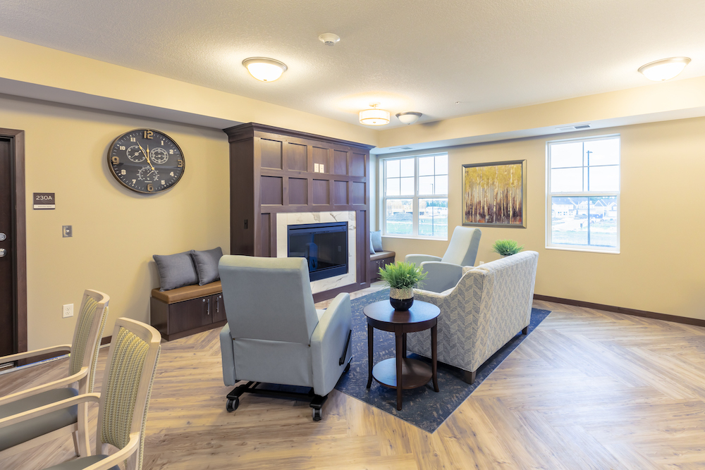 Cozy lounge area with chairs and a sofa arranged around a modern fireplace in a brightly lit room.