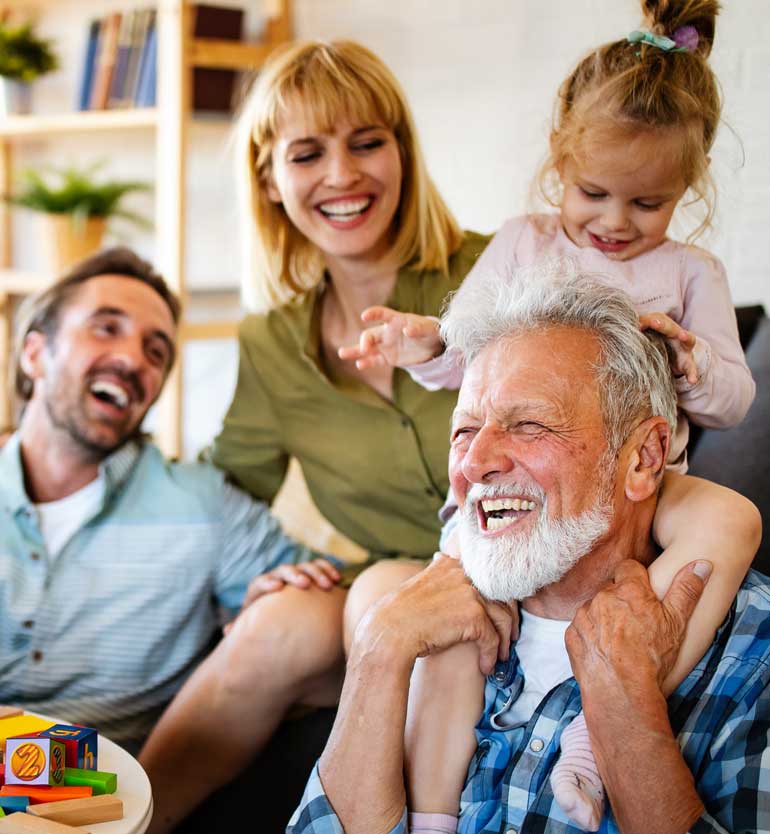senior-with-family Senior man joyfully playing with his family, including a child on his shoulders and two adults laughing.