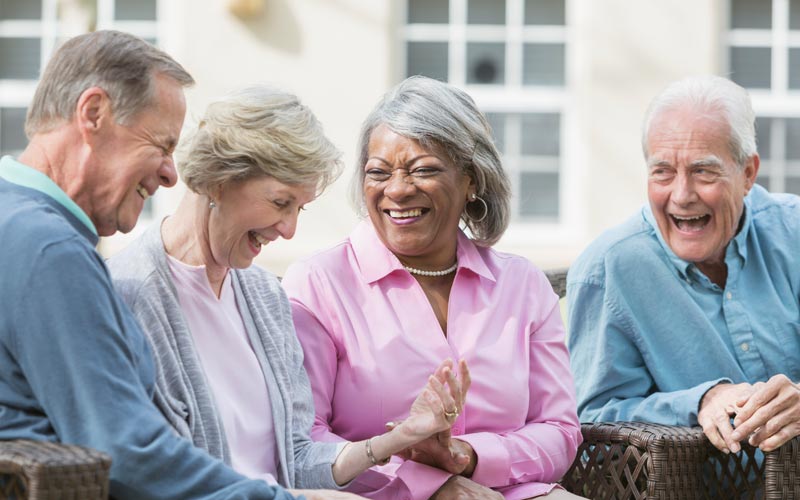 lcs-signature-programs Four senior adults laughing and enjoying conversation while seated outdoors, showcasing active aging.